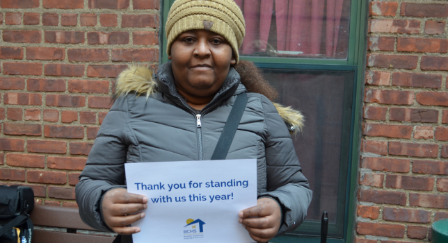 An individual standing outside holds a paper sign that says "Thank you for standing with us this year!" and the BCHS logo.