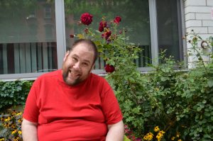 An individual smiling, sitting in front of a garden